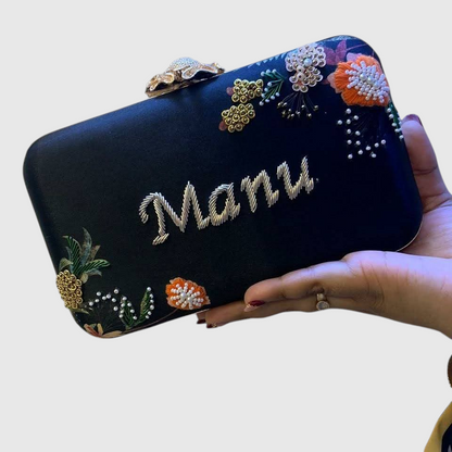 Cannish Pitara black personalized clutch with hand-embroidered Manu name and floral beadwork held in a hand
