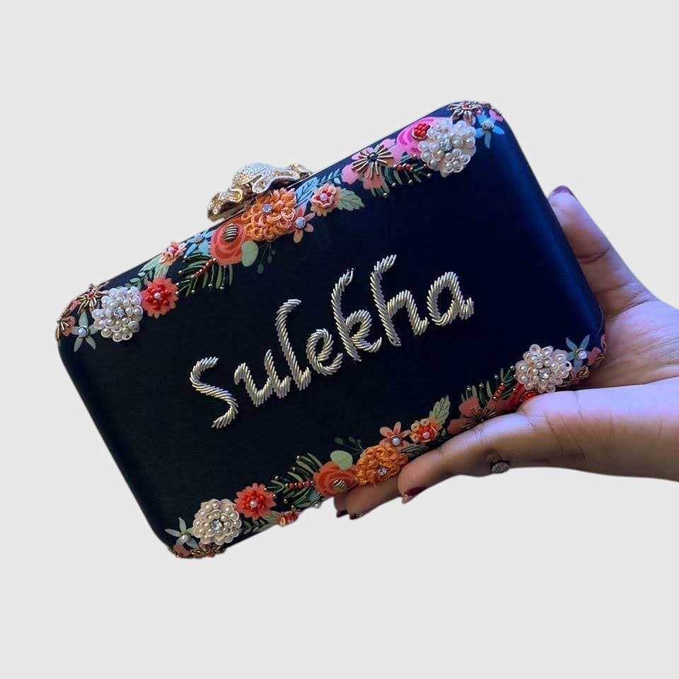 Cannish Pitara black personalized clutch with Sulekha name embroidery, floral handwork, and metallic clasp.